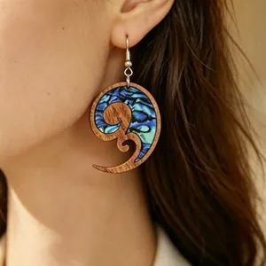 Dettaglio di orecchini a spirale in legno con intarsio in conchiglia blu.