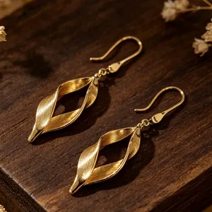 Vista detallada de pendientes de hojas doradas con diseño de espiral en madera.