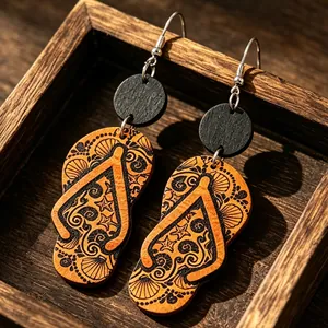 Primer plano de pendientes de madera con forma de chancla y motivos de playa y conchas