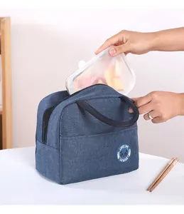 Detailed view of placing a food container into a blue insulated Oxford cloth lunch bag