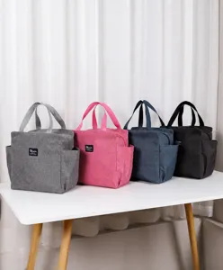 Sélection de quatre sacs à lunch isolés en gris, rose, bleu et noir sur une table blanche.