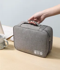 Mano sosteniendo un organizador de accesorios electrónicos gris sobre un escritorio