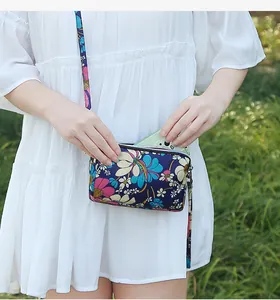 Close-up detail of a floral crossbody phone bag with three zipper compartments in use