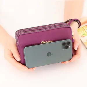 Bolso de mano de nailon morado para móvil con triple cremallera y detalle dorado.