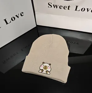 Close-up detail of beige knitted beanie with cute embroidered capybara cartoon character