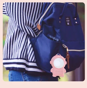 Pink astronaut cartoon hand warmer with USB charging hanging on a blue backpack detail.
