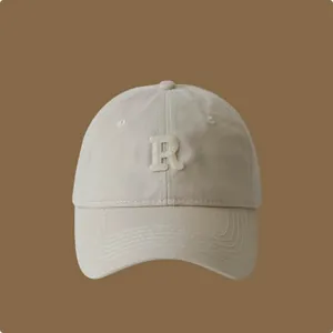 Dettaglio ravvicinato di un cappellino da baseball beige in cotone con lettera R ricamata.