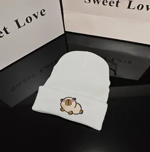Detail of white knit beanie hat featuring cute cartoon capybara embroidery design