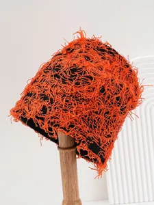 Detailed view of an orange and black distressed knit beanie shown on a wooden stand