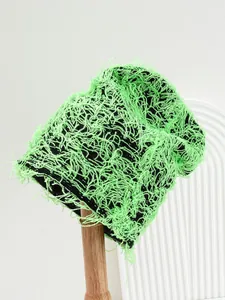Close-up macro detail of vibrant green distressed frayed knit beanie on a wooden stand