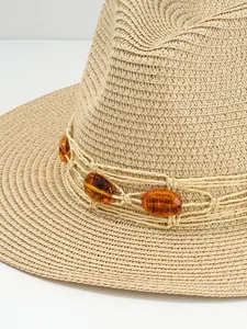 Close-up detail of straw hat with elegant amber gemstone beads on the woven band