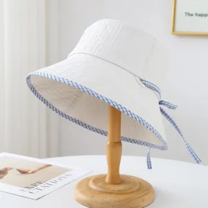 Vue détaillée d'un chapeau cloche blanc avec ruban à carreaux bleus sur support.