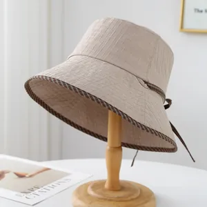 Détail d'un chapeau bob beige texturé avec un nœud en ruban marron sur socle en bois