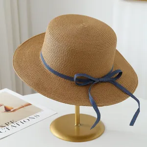 Handmade raffia straw sun hat featuring a blue denim bow accent on a gold display stand