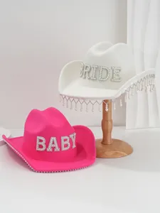 Macro detail of white Bride and pink Baby felt cowboy hats with rhinestone letters.
