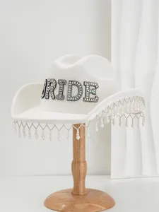 Detail view of a white wool cowboy hat with rhinestone 'BRIDE' and pearl fringe.