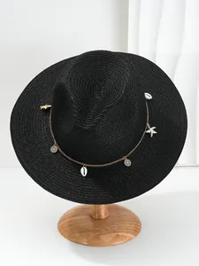 Close-up van zwarte strohoed met schelp en zeester gouden ketting decoraties.