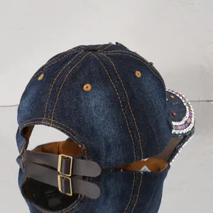 Detailansicht einer Jeans-Baseballkappe mit bunten Strasssteinen und Lederarmband