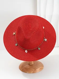Detailopname van een rode strohoed met zeesterren, schelpen en een gouden ketting.