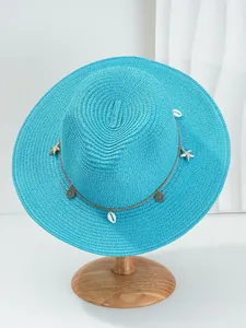 Detailweergave van blauwe strooien Panama-hoed met bedeltjes van schelpen en zeesterren op ketting