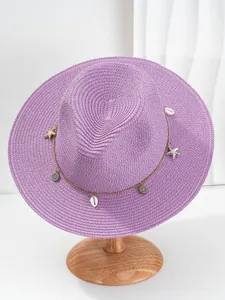Detail van een paarse Panama strohoed met schelp- en zeesteraccessoires op houten standaard.