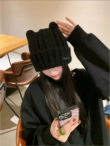 An Asian model wearing a cute black knit cat ear beanie in a cozy cafe setting.