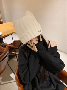 Detailed view of white knit cat ear beanie with textured pattern and metal tag