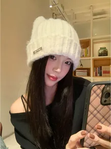 Close-up view of a cozy white knit beanie hat with cute cat ears worn by a model.