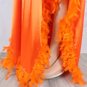Detailaufnahme der orangefarbenen Satinrobe mit Federbesatz und hohem Schlitz.
