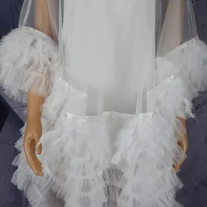 Detailed view of white mesh dress with delicate feather trim and tiered tulle layers.