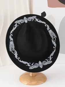 Detail view of a black vintage fedora hat with white moth and vine embroidery patterns