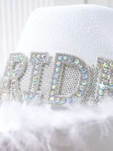 Close-up of iridescent BRIDE rhinestone lettering on a white bridal feather hat.
