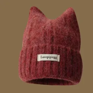 Close-up of a burgundy knitted beanie with cute cat ears and a decorative brand label