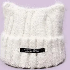 Close-up of white cat ear beanie with fluffy texture and black Rose will bloom tag.