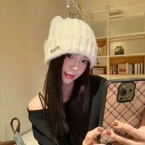 Cute white knitted cat ear beanie hat worn by a model in a warm indoor setting