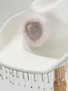 Close-up of a white cowboy hat featuring a pink furry rhinestone heart and tassel fringe