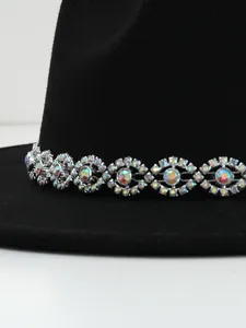 Close-up detail of the eye-shaped iridescent gemstone accessory on a black felt fedora hat