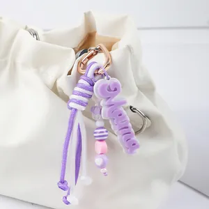 Handmade purple braided bag charm featuring Mama tag and beads attached to a white bag