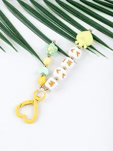 Close-up of MAMA silicone beaded bag charm with yellow heart clasp and palm leaf background
