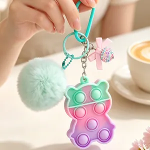 Colorful bear-shaped pop-it keychain featuring a mint green pompom and bow charm decoration.