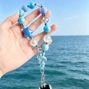 Detail van blauw kralen telefoonkoord met sterbedel tegen de oceaanachtergrond.