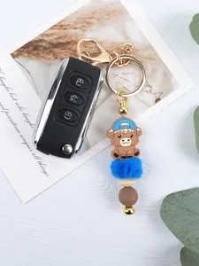 Close-up of cartoon cow keychain with blue pom-pom and silicone beads decoration.