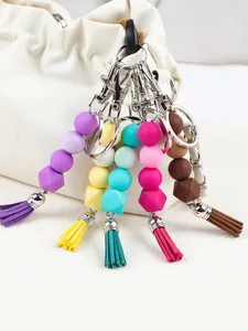 Detail view of multiple colorful silicone bead keychains with tassels hanging on a white bag.