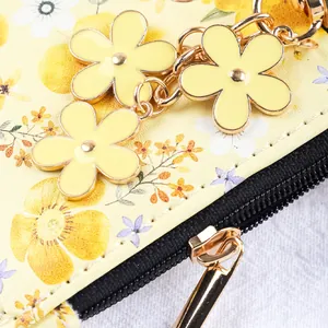 Vue détaillée d'un porte-monnaie à fleurs jaunes avec breloques en émail et fermeture éclair.