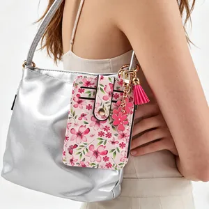 Détail d'un porte-cartes à fleurs roses avec gland attaché à un sac argenté.