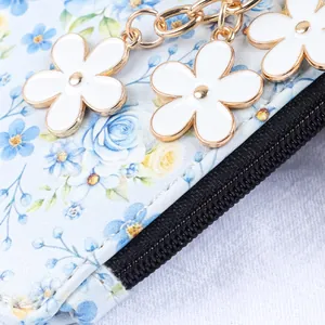 Détail d'un porte-cartes à imprimé floral avec breloques fleurs blanches et fermeture éclair.