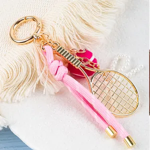 Vista detallada de un llavero de raqueta de tenis dorado con cordón trenzado rosa.
