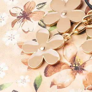Détail rapproché du pendentif fleur en émail beige et du porte-cartes à motif floral chic.