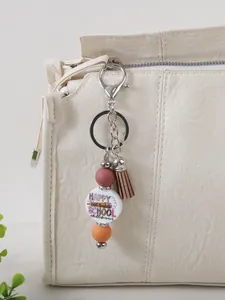 Macro detail of silicone bead keychain with tassel hanging on a stylish white textured bag