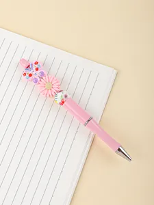 Close-up of pink beaded ballpoint pen with butterfly and flower charm on notebook